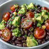 Serving suggestion of a vibrant Black Bean and Veggie Bowl topped with creamy avocado and crunchy pumpkin seeds on a rustic table.