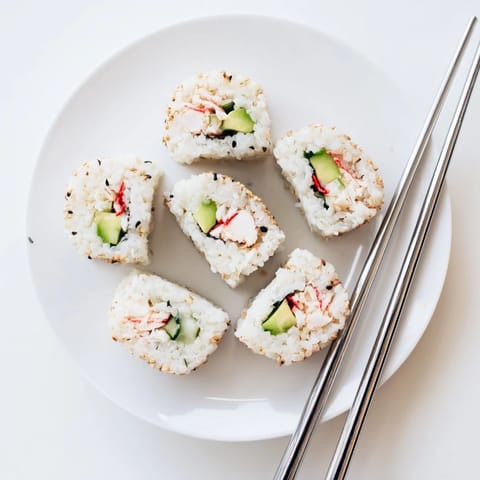 Chilled California Roll pieces topped with sesame seeds, served with soy sauce, ginger, and wasabi on a plate.