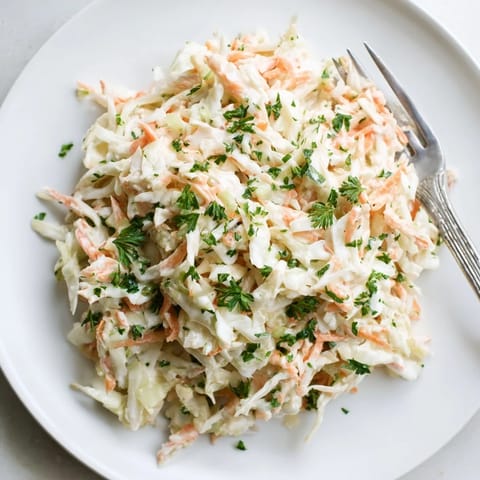 Homemade Coleslaw with Apple salad in a bowl, topped with parsley, served chilled alongside grilled chicken.