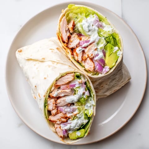 Smoky Chipotle Chicken Wrap sliced in half, revealing layered ingredients inside a soft tortilla.  