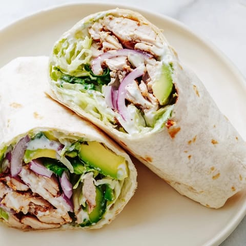 Freshly assembled Smoky Chipotle Chicken Wrap with grilled chicken, avocado, and crisp lettuce.  