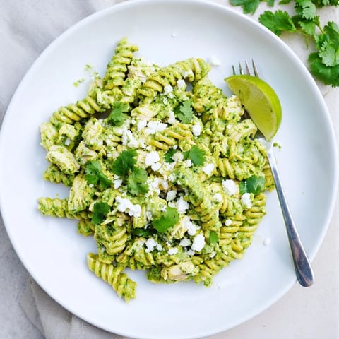 Shredded chicken and rotini coated in vibrant green cilantro-lime yogurt sauce, served warm with crumbled feta cheese for a fresh, zesty meal.