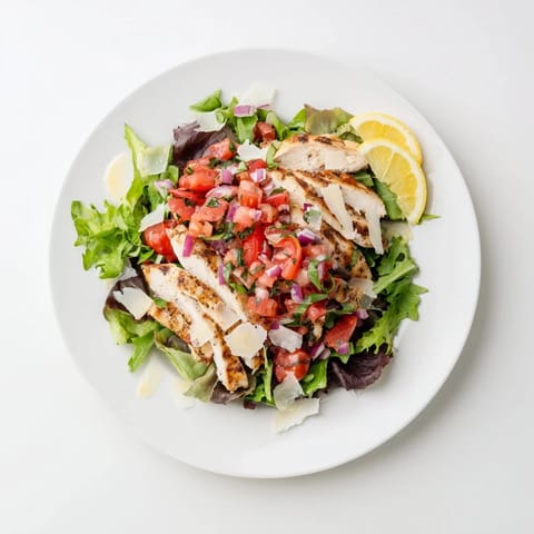 Platter of bruschetta chicken salad with juicy grilled breasts, red onion, and shaved Parmesan, served with bright lemon wedges.