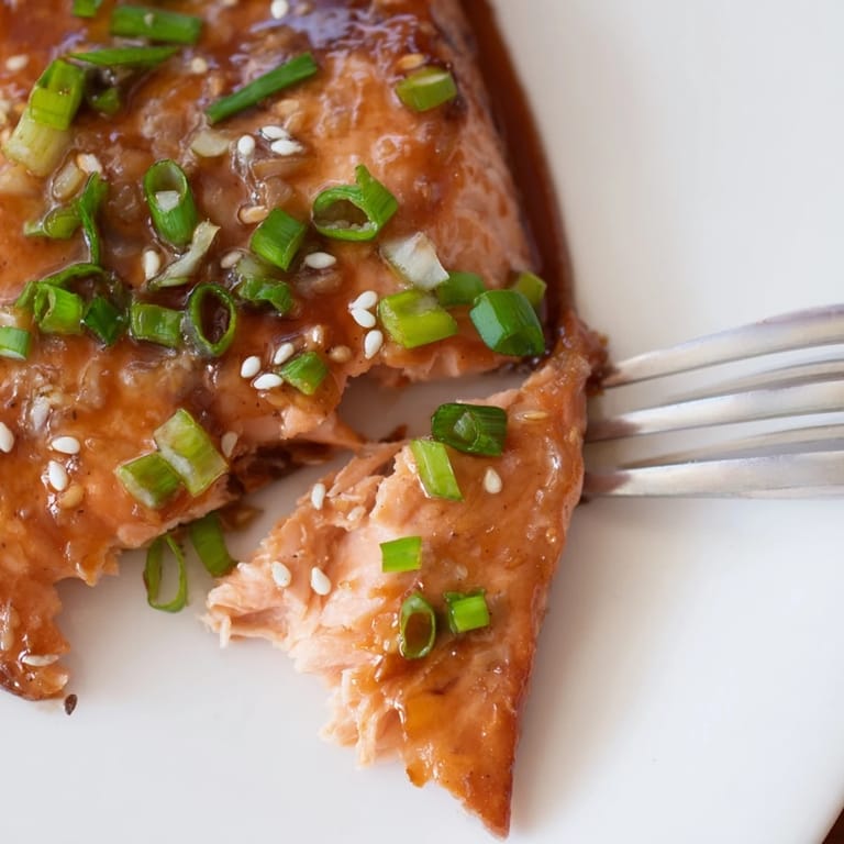 Close-up of a glazed honey garlic salmon fillet with a spoon drizzling thick, sweet-savory sauce over the top.