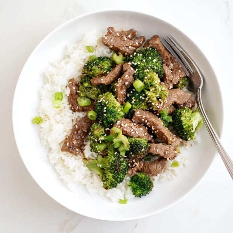 Classic homemade Beef and Broccoli plated with jasmine rice and topped with fresh sliced green onions.