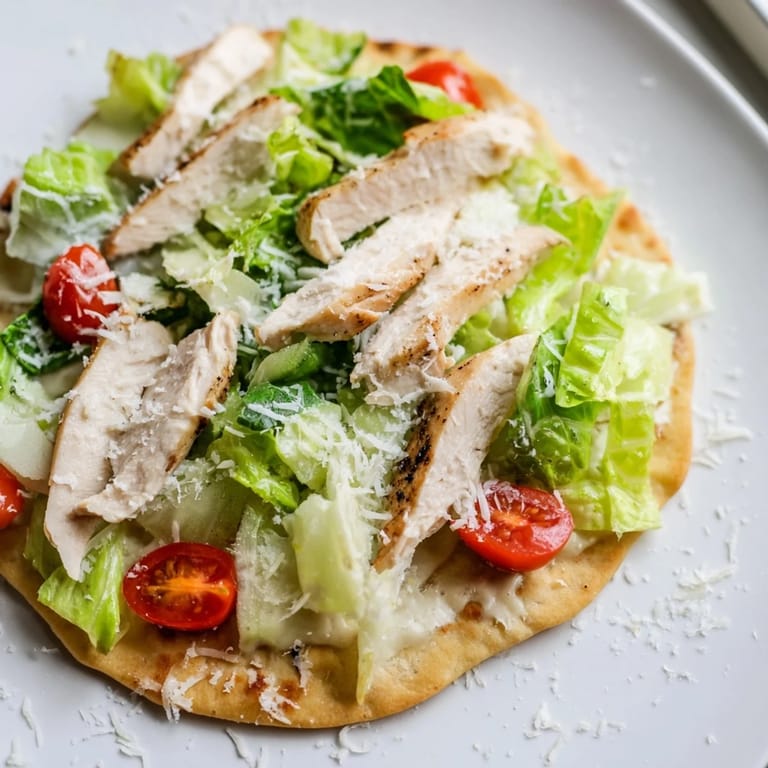 Warm Chicken Caesar Flatbread served with juicy sliced chicken, creamy dressing, and fresh cherry tomatoes for a light lunch.  