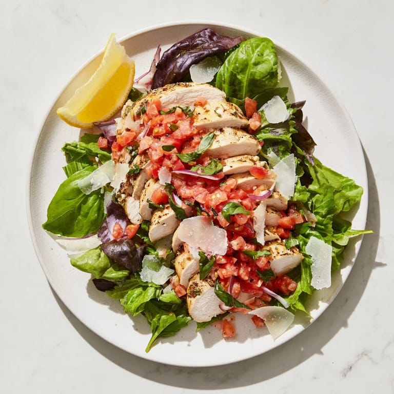 Close-up of a bruschetta chicken salad bowl, showcasing glistening tomato-basil bruschetta over crisp greens, ready for a light, low-carb meal.