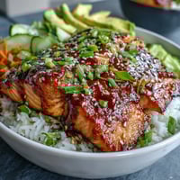 1. A colorful teriyaki salmon bowl with glazed salmon fillets, fresh cucumber, avocado, and carrot on jasmine rice, garnished with sesame seeds.  